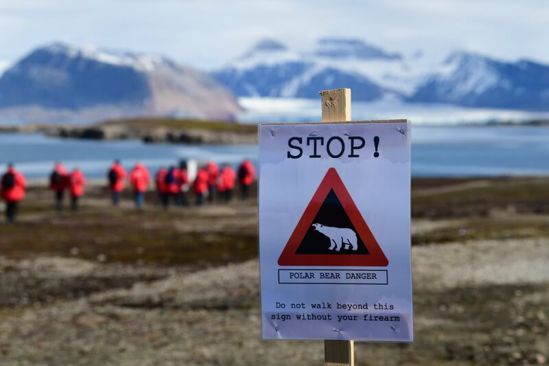 Warnschild mit Eisbär und dem Hinweis ab diesem Punkt nur noch mit Schusswaffen unterwegs zu sein